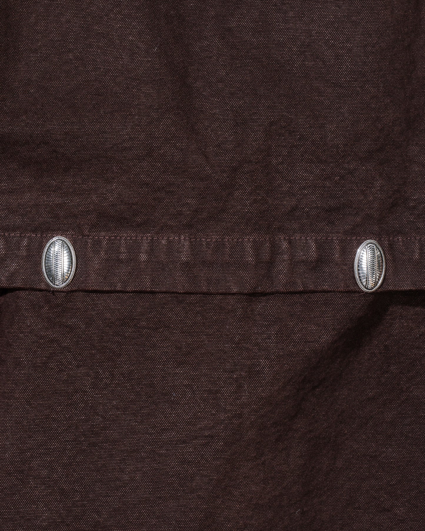 Close-up of a brown fabric with metal buttons on a dark background