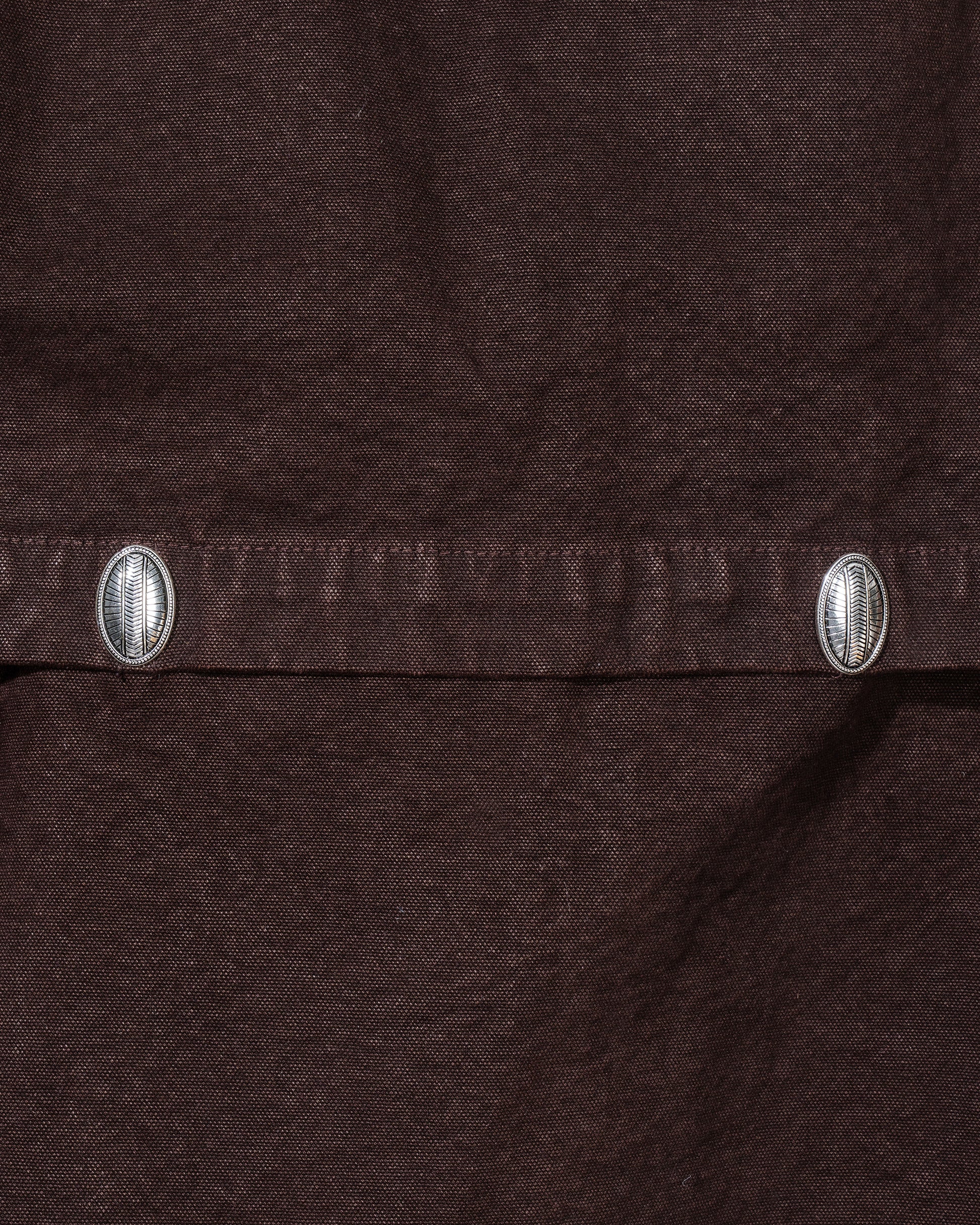 Close-up of a brown fabric with metal buttons on a dark background